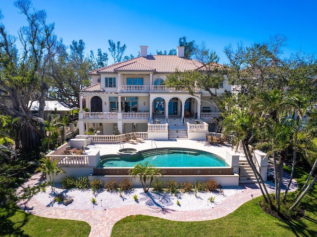 rear view of property featuring a balcony, a tile roof, a chimney, stairs, and a patio area