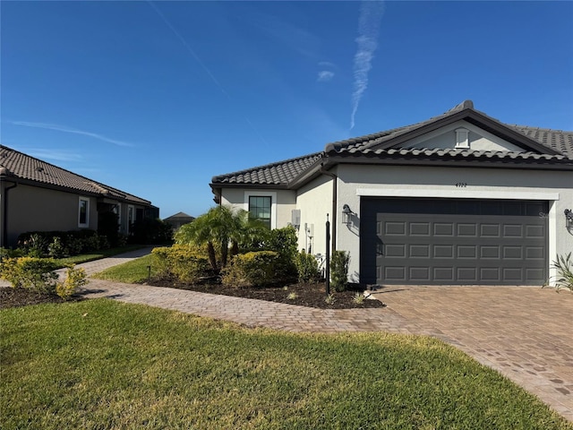 ranch-style home featuring a tile roof, an attached garage, decorative driveway, a front lawn, and stucco siding