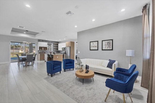 living area featuring a tray ceiling, recessed lighting, visible vents, and baseboards