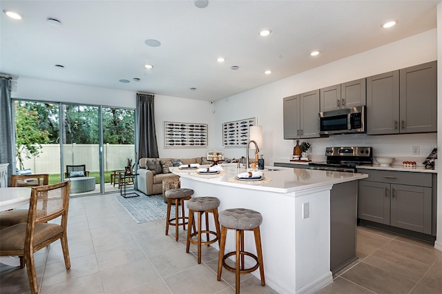 kitchen with a breakfast bar, a sink, appliances with stainless steel finishes, gray cabinets, and a center island with sink