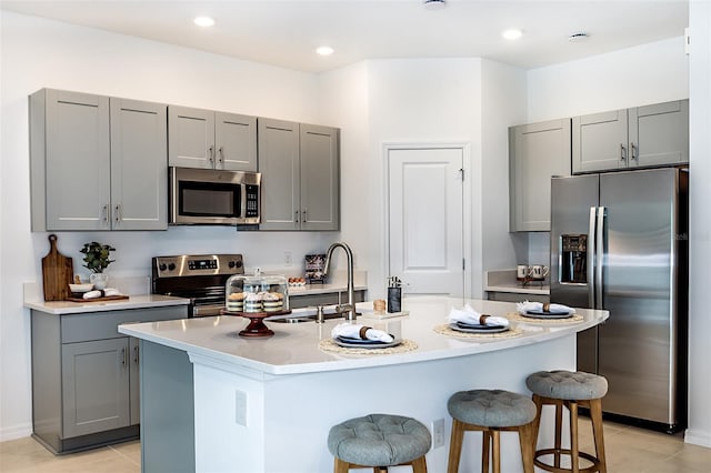 kitchen featuring gray cabinetry, stainless steel appliances, a sink, a kitchen breakfast bar, and light countertops