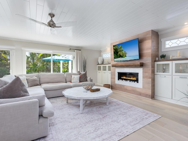 living area with light wood-type flooring, ceiling fan, a fireplace, and ornamental molding