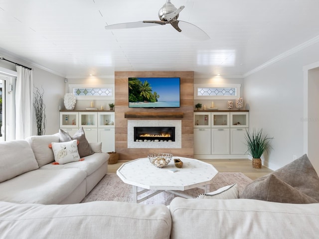 living area featuring light wood-type flooring, ceiling fan, a fireplace, and ornamental molding