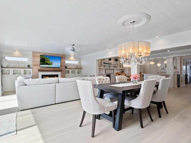 dining area featuring built in shelves, crown molding, recessed lighting, light wood-style floors, and a large fireplace