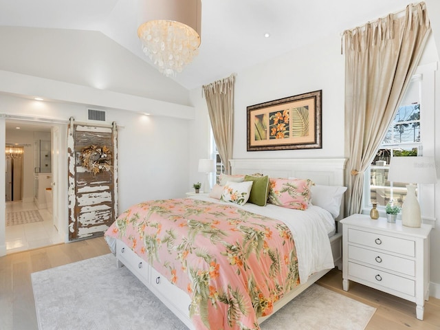 bedroom with a notable chandelier, visible vents, light wood-style flooring, a barn door, and vaulted ceiling