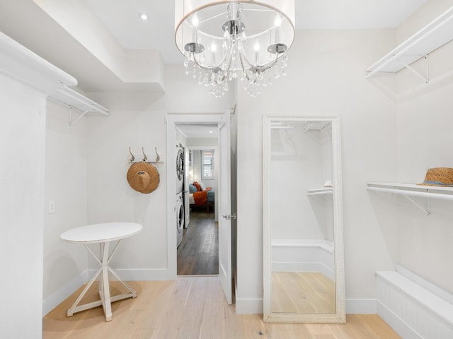 spacious closet with stacked washing maching and dryer, wood finished floors, and a notable chandelier