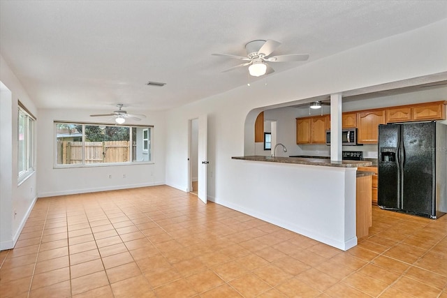 kitchen featuring visible vents, black fridge, brown cabinets, stainless steel microwave, and dark countertops