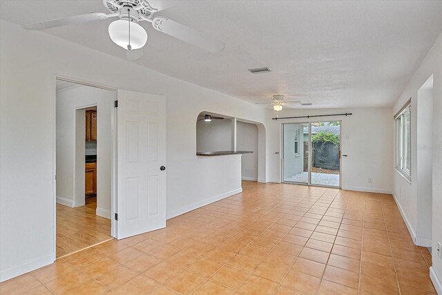 empty room with light tile patterned floors, arched walkways, visible vents, a ceiling fan, and baseboards