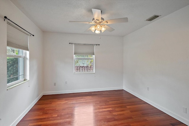 spare room with a textured ceiling, wood finished floors, visible vents, and baseboards