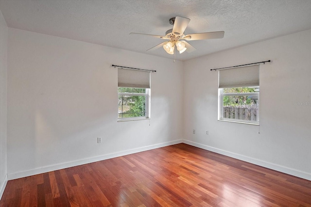 unfurnished room featuring a textured ceiling, wood finished floors, a wealth of natural light, and baseboards