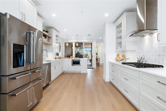 kitchen with open shelves, a sink, light countertops, appliances with stainless steel finishes, and wall chimney range hood