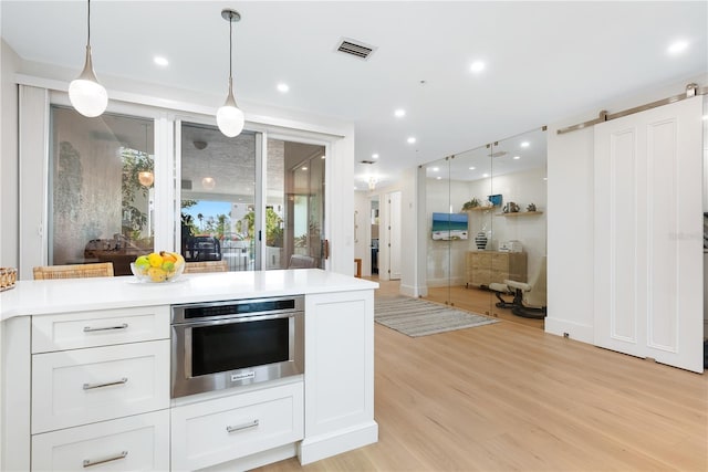 kitchen featuring light wood finished floors, light countertops, white cabinetry, stainless steel oven, and decorative light fixtures