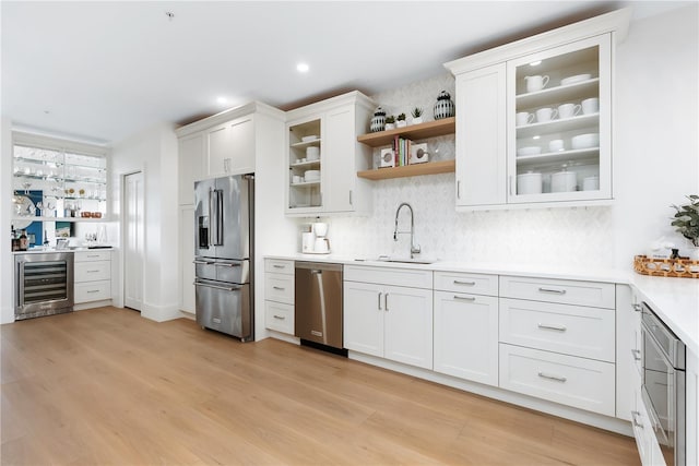 kitchen featuring light wood-style flooring, beverage cooler, a sink, appliances with stainless steel finishes, and light countertops