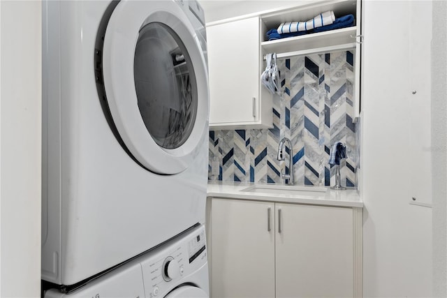 laundry area with stacked washer / dryer, cabinet space, and a sink