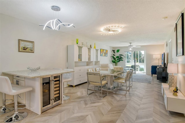 dining area featuring wine cooler, a textured ceiling, and ceiling fan with notable chandelier