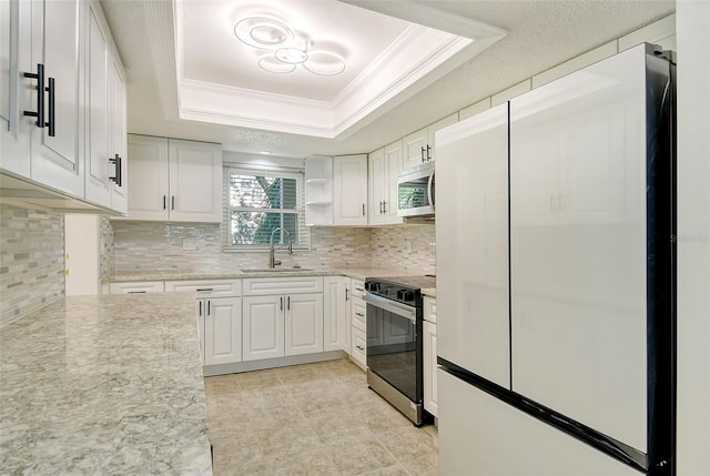 kitchen with a sink, electric stove, freestanding refrigerator, a tray ceiling, and stainless steel microwave