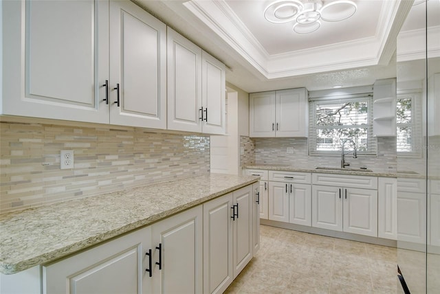 kitchen with crown molding, a raised ceiling, decorative backsplash, white cabinetry, and a sink