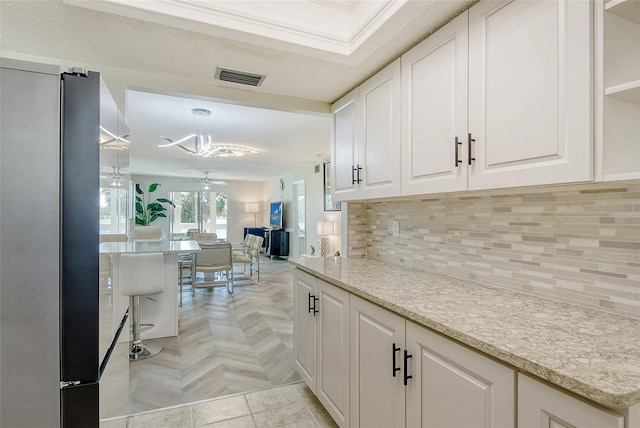 kitchen with a ceiling fan, white cabinets, open floor plan, visible vents, and decorative backsplash