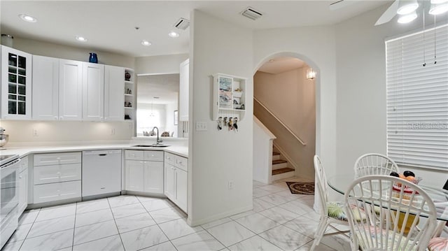 kitchen featuring visible vents, white cabinets, arched walkways, white dishwasher, and a sink