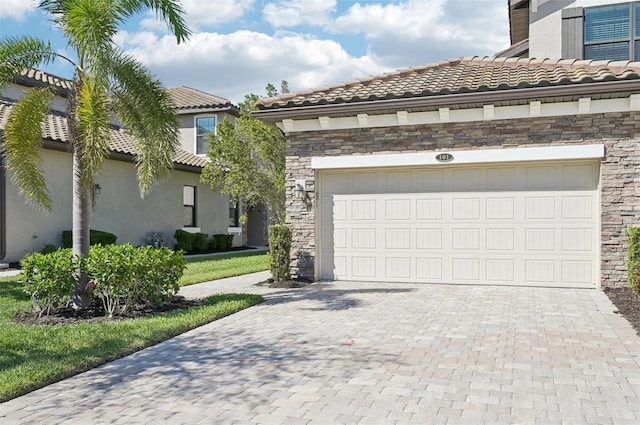 view of front of house with stone siding, a tile roof, an attached garage, decorative driveway, and stucco siding