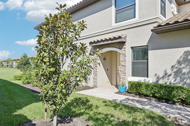 property entrance with a yard, a tile roof, stone siding, and stucco siding