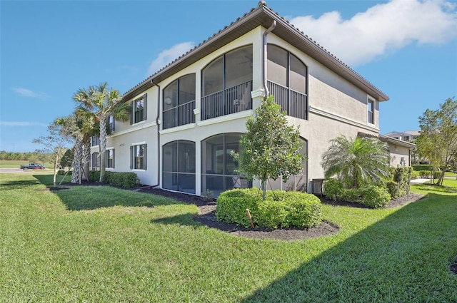 rear view of house featuring a sunroom, stucco siding, and a yard