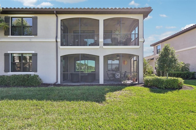 rear view of house featuring stucco siding, a sunroom, and a yard