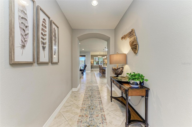 hallway featuring arched walkways, an inviting chandelier, baseboards, and light tile patterned floors