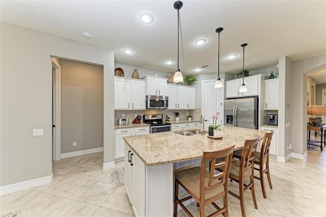 kitchen with light tile patterned floors, stainless steel appliances, a sink, tasteful backsplash, and a center island with sink