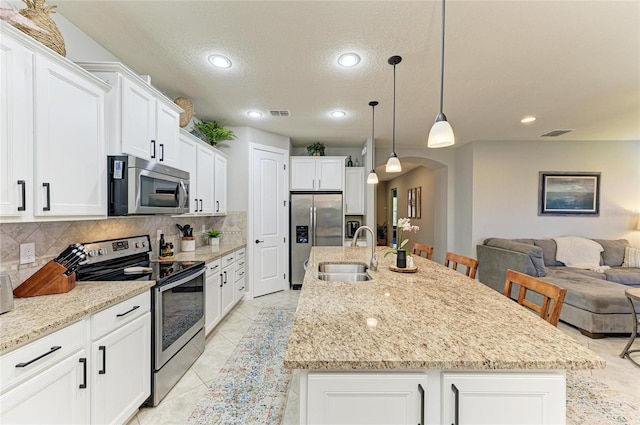 kitchen featuring arched walkways, open floor plan, a sink, stainless steel appliances, and backsplash