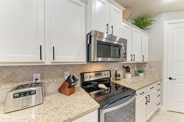 kitchen featuring light tile patterned floors, light stone counters, white cabinetry, appliances with stainless steel finishes, and backsplash