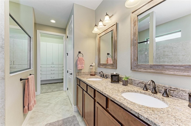 bathroom featuring tile patterned floors, tiled shower, a sink, and double vanity