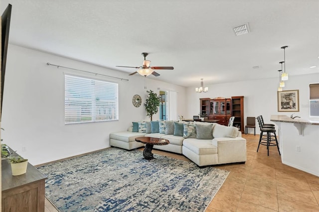 living room featuring light tile patterned floors, visible vents, baseboards, and ceiling fan with notable chandelier