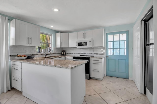 kitchen featuring light tile patterned floors, electric range, decorative backsplash, white microwave, and a sink