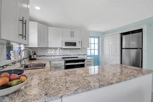 kitchen with white microwave, a sink, freestanding refrigerator, light stone countertops, and electric range oven