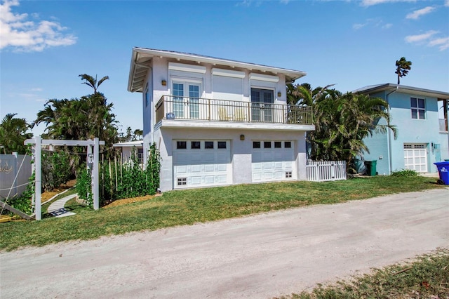 view of front of property featuring french doors, stucco siding, fence, a balcony, and a garage