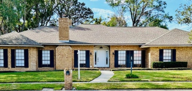 view of front of home featuring brick siding, a chimney, a front lawn, and roof with shingles