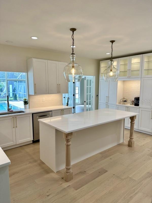 kitchen with tasteful backsplash, dishwasher, light countertops, light wood-style flooring, and a sink