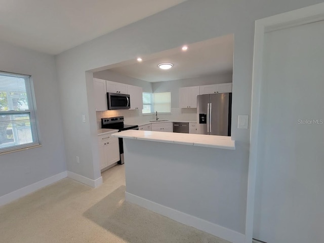 kitchen with stainless steel appliances, light countertops, white cabinetry, a sink, and baseboards