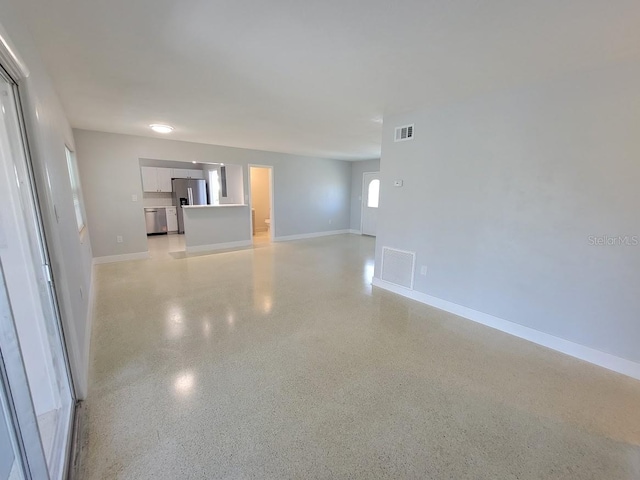 unfurnished living room featuring light speckled floor, visible vents, and baseboards