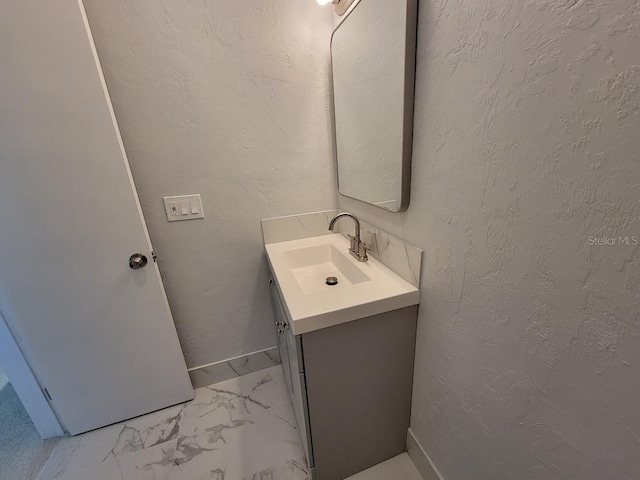 bathroom featuring marble finish floor, vanity, baseboards, and a textured wall