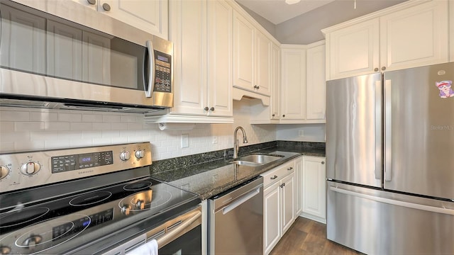 kitchen with a sink, backsplash, dark stone counters, appliances with stainless steel finishes, and white cabinets