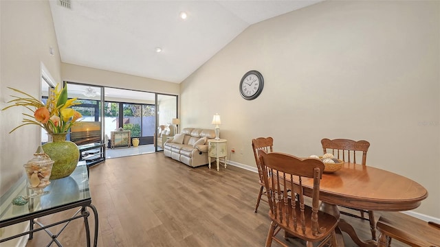 dining room featuring visible vents, wood finished floors, baseboards, and high vaulted ceiling