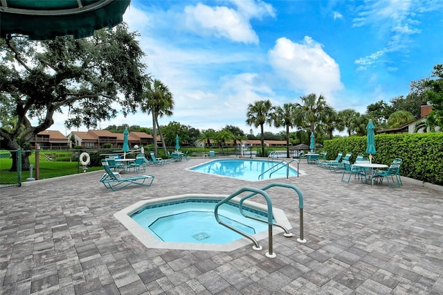 pool with a patio area, a community hot tub, and fence