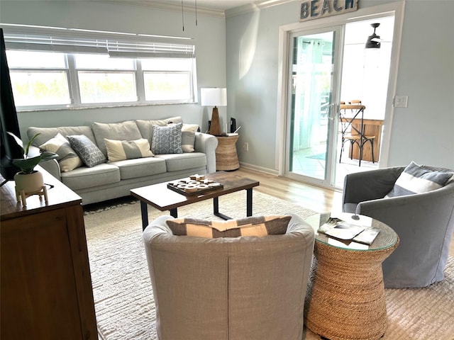 living area featuring baseboards, light wood-style floors, a ceiling fan, and crown molding