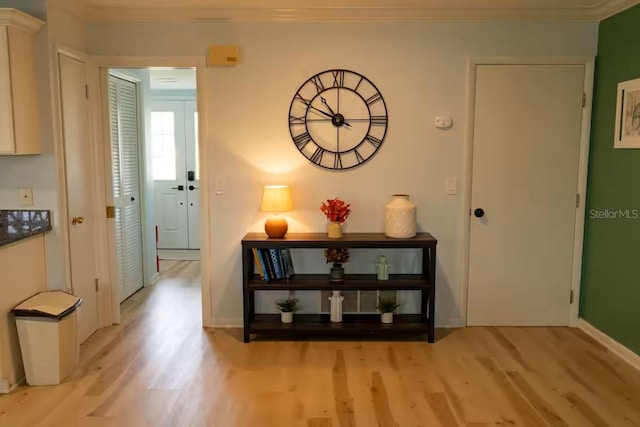 hall featuring light wood-type flooring, crown molding, and baseboards