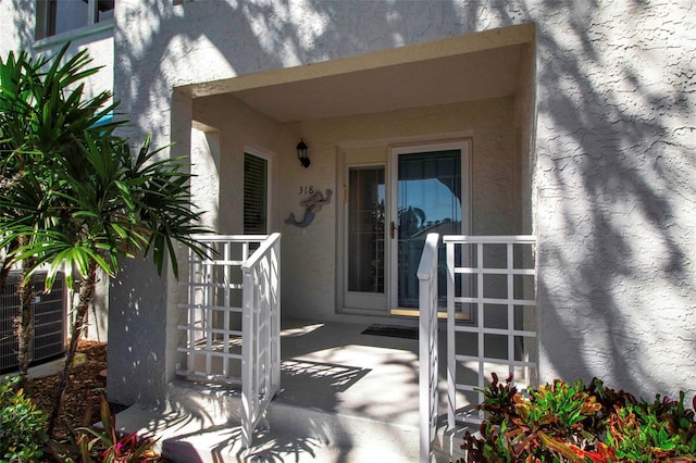 view of exterior entry with central air condition unit and stucco siding