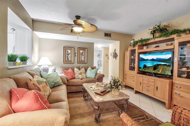 living room with light tile patterned floors, ceiling fan, visible vents, and a textured ceiling