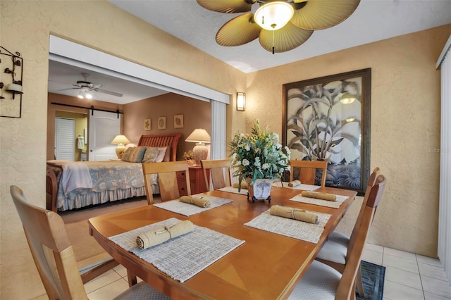 tiled dining room with ceiling fan, a textured wall, and a barn door