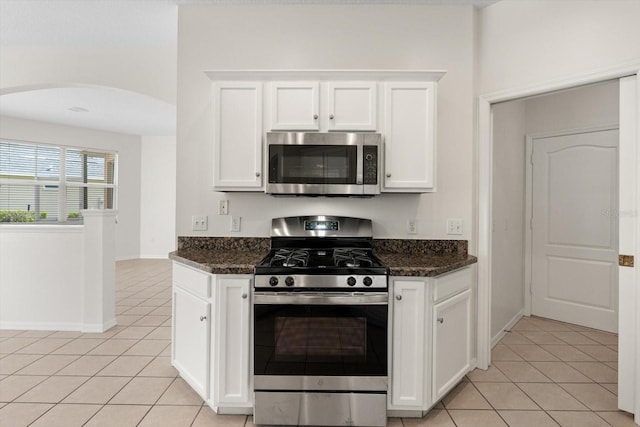 kitchen with appliances with stainless steel finishes, arched walkways, white cabinets, and light tile patterned floors